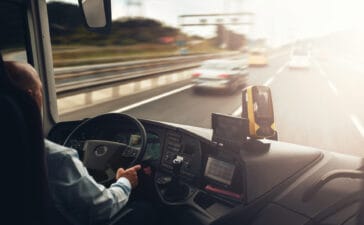 Image of a bus driver from behind, driving down a highway at sunset