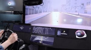 A hands-on driving simulation with a visible dashboard and a screen displaying a city street scenario in progress.