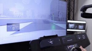 A simulated urban intersection with cognitive load metrics shown on the screen, traffic signals visible, and dashboard controls in a driving simulation environment.