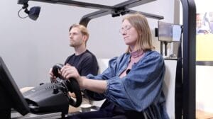 Two participants engaging in a driving simulation experience, focusing on the road while demonstrating the usability and in-cabin interaction of the simulator.
