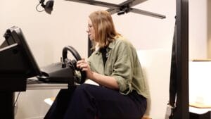 A person interacting with a driving simulator to test interior sensing systems, including gaze detection, posture monitoring, and driver attentiveness tracking.