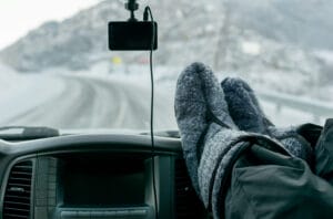 Person in warm boots in a dangerous seating position, with their feet on the dashboard of the car