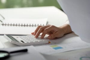 Close-up of a hand using a calculator over financial reports, symbolizing cost analysis and budget planning for investing in eye tracking systems.